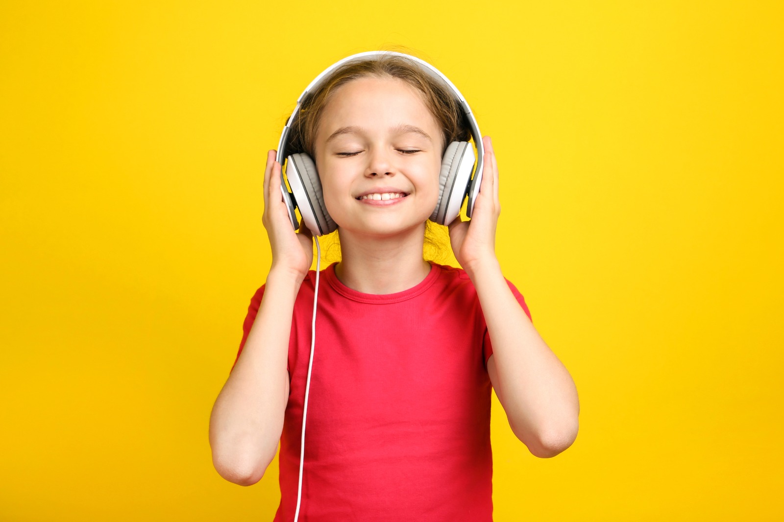 Happy girl enjoying music with headphones against a yellow background.