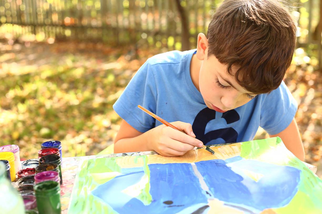 Child painting outdoors at a table with colorful paints – Westminster Arts Academy