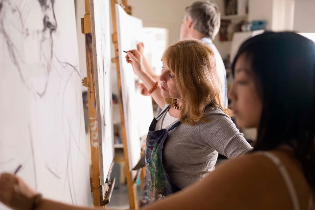 Adult students participating in an art class, painting on canvases in a bright and creative studio environment